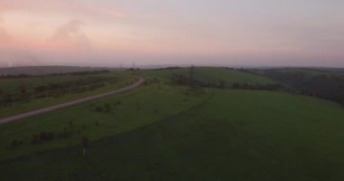 Havadan görünümü. kırsal manzara ile yeşil tepeler geçen uzun ve dolambaçlı yolu. Hava kirliliği sanayi kenti çevresinde. 4k