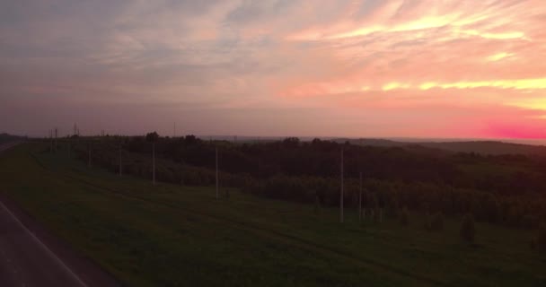 Luchtfoto. lange en bochtige weg langs groene heuvels met platteland landschap bij zonsondergang. 4k — Stockvideo