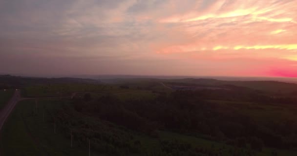 Luchtfoto. lange en bochtige weg langs groene heuvels met platteland landschap bij zonsondergang. 4k — Stockvideo