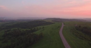Havadan görünümü. kırsal manzara ile yeşil tepeler geçen uzun ve dolambaçlı yolu. Hava kirliliği sanayi kenti çevresinde. 4k