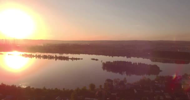 Vista aérea. puesta de sol sobre el lago con la pequeña ciudad en una orilla. Planta industrial en un horizonte. 4K — Vídeo de stock