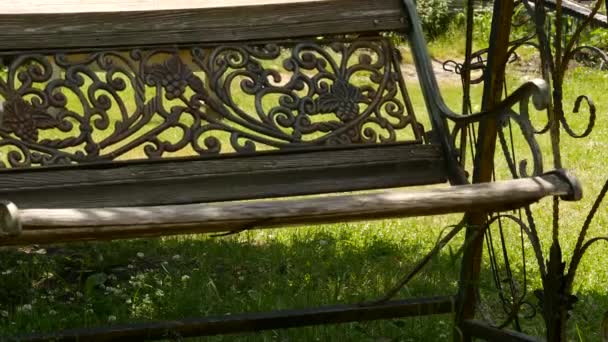 Пустые выкованные старые качели, раскачивающиеся в зеленом саду. покинутая концепция сада. 4K — стоковое видео