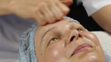kadın doktor istemciye anti-aging masaj yapıyor. kadın plastik yüz masaj spa saton sahiptir. 4k