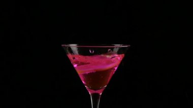 limon parçası karanlık bir arka plan üzerinde pembe kokteyl ile bir bardak içine atılır. ağır çekim
