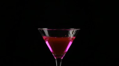 limon parçası karanlık bir arka plan üzerinde pembe kokteyl ile bir bardak içine atılır. ağır çekim