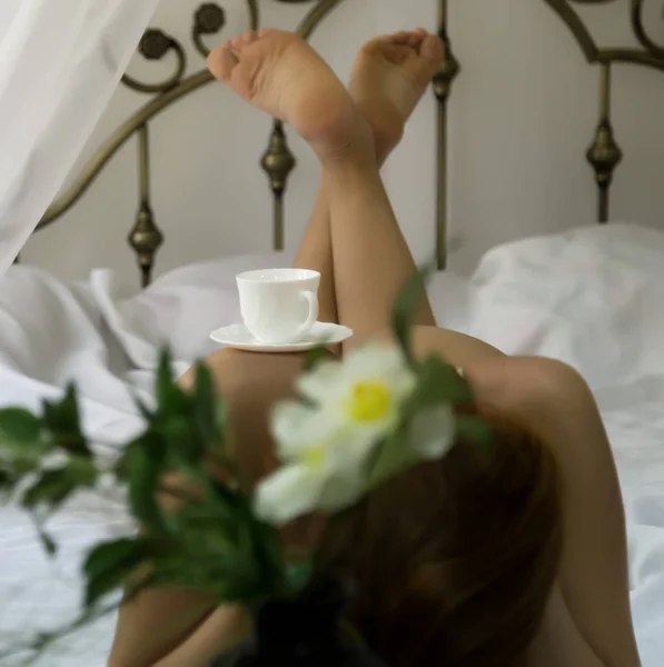 Сексуальна гола жінка розслабляється на ліжку з чашкою чаю на її сідницях — стокове фото