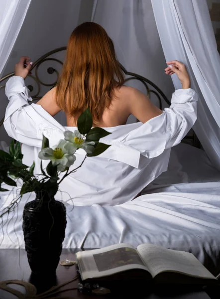 침대에 앉아 흰 셔츠에 긍정적인 섹시 한 여자의 뒷면 — 스톡 사진