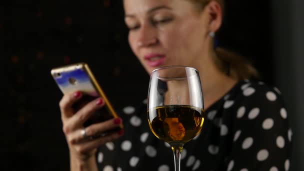 携帯電話で話していると、暗闇の中でワインを飲む幸せな女。お祭りの雰囲気とお祝いのコンセプトです。スローモーション — ストック動画