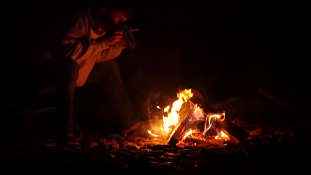 Skäggiga män dricker te från stora koppen och göra ett foto på en mobiltelefon av brasa i en mörk. 4k — Stockvideo