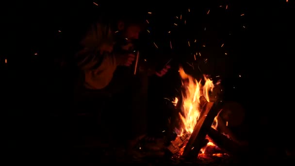 Bearded men drink tea from big cup and make a photo on a cellphone of bonfire in a dark. 4K — Stock Video