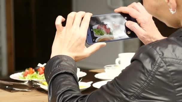 Жінка у відкритому кафе фотографує їжу зеленим салатом і чашкою кави. повільний рух — стокове відео