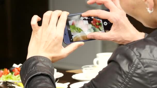 Woman in outdoor cafe takes a picture of food green salad and cup of coffee. 4K — Stock Video