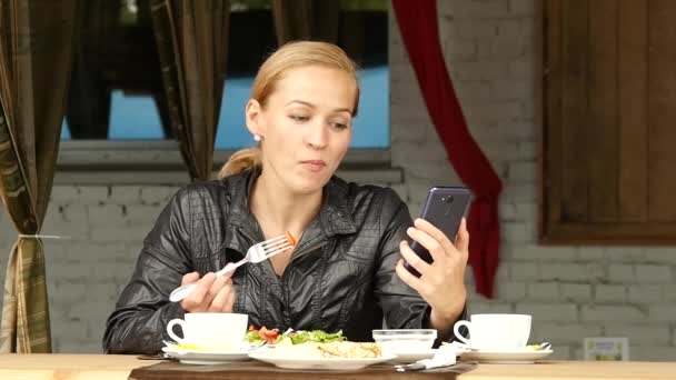 女商人在户外咖啡馆里吃沙拉。女孩吃绿色美味的食物和检查电子邮件在您的电话。慢动作 — 图库视频影像