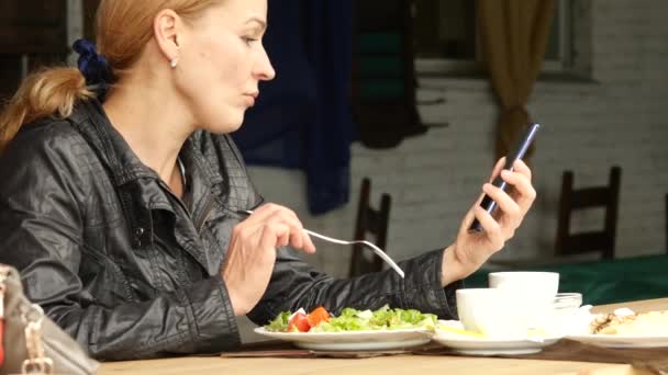 Бізнес-леді їсть салат у відкритому кафе. дівчина їсть зелену смачну їжу і перевіряє електронну пошту на вашому телефоні. повільний рух — стокове відео