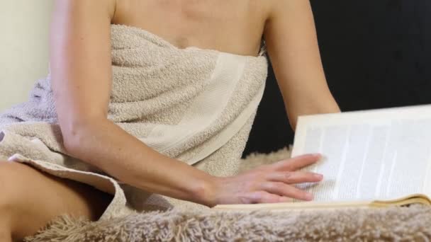 Mulher atraente em uma toalha de banho lendo um livro. Menina bonita descansando confortavelmente em uma cama. 4K — Vídeo de Stock