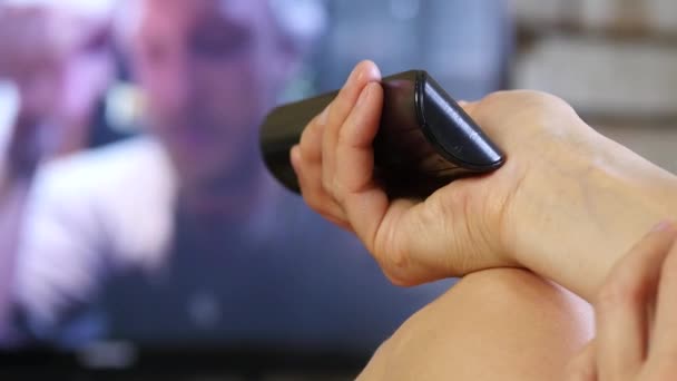 Mujer atractiva viendo la televisión y cambia de canal. chica después de la ducha envuelta en una toalla. 4K — Vídeos de Stock