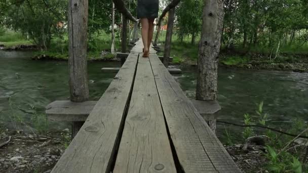 Joven mujer están caminando a lo largo de un estrecho puente de madera sobre un río de montaña. concepto de camping y aventura — Vídeos de Stock