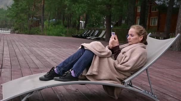 Jonge vrouw ontspannen in de leunstoel in de buurt van berg rivier en surfen op smart phone — Stockvideo