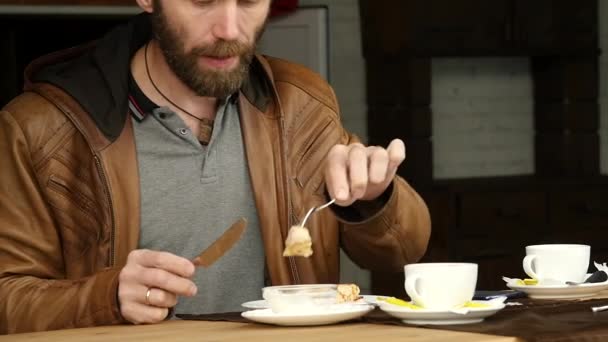 Der bärtige Mann frühstückt auf der Terrasse eines Cafés im Freien. Zeitlupe — Stockvideo