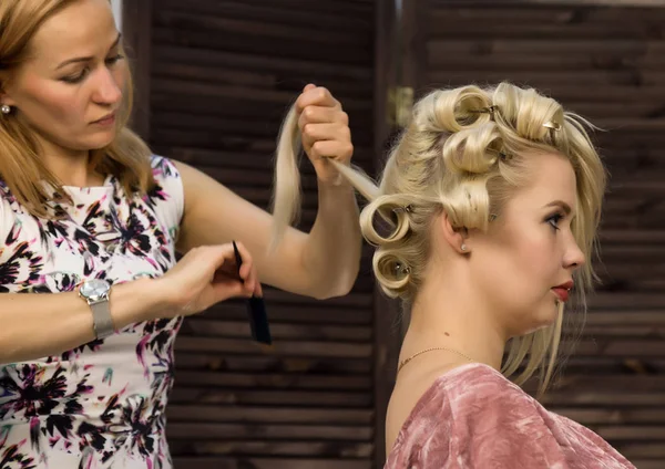 Hairdresser does hairstyle for luxurious blond woman. coiffure in the form of big curl. Concept wedding hairstyle