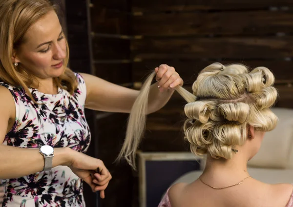 Парикмахер делает прическу для роскошной блондинки. coiffure in the form of big curl. Концепция свадебной прически — стоковое фото