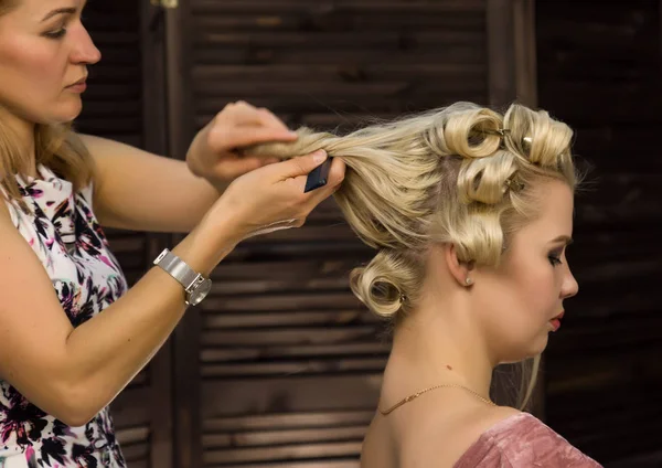 elegant blonde woman in beauty saloon. Hairdresser does coiffure in the form of big curl. Concept wedding hairstyle
