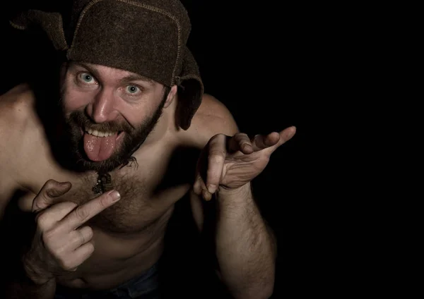 frightening bearded man showing middle finger. strange Russian man with a naked torso and a woolen hat. free space for your text