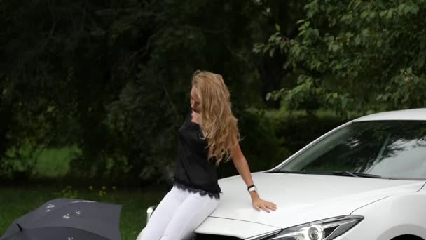 Blondynka młoda kobieta siedzi na kaptur biały samochód w letni dzień. zwolnionym tempie — Wideo stockowe