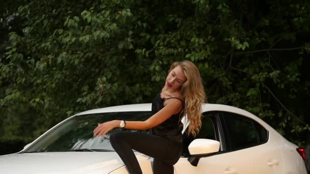 Hermosa joven rubia con el pelo largo de pie cerca de coche blanco . — Vídeo de stock