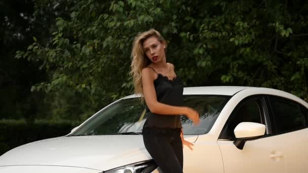 Красивая молодая блондинка с длинными волосами стоит рядом с белой машиной . — стоковое видео