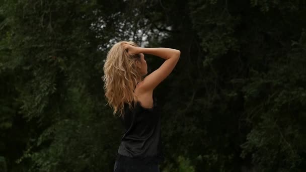 Вид ззаду на блондинку на фоні природи. Красива дівчина позує з літаючим волоссям. повільний рух — стокове відео