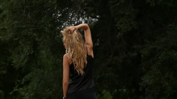 Vista posteriore della donna bionda sullo sfondo della natura. Bella ragazza posa con i capelli volanti. rallentatore — Video Stock