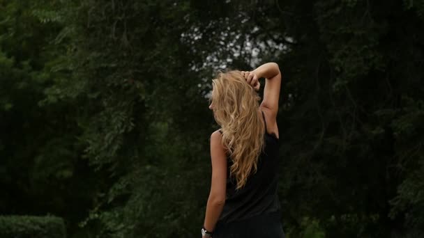 Achteraanzicht van blonde vrouw op natuur achtergrond. Mooi meisje vormt met haar vliegende. Slow motion — Stockvideo