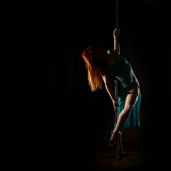 Striptease dansen met een paal in de nachtclub. Prachtige sexy vrouw in een lange turquoise jurk met een gleuf op een donkere achtergrond. vrije ruimte voor uw tekst — Stockfoto