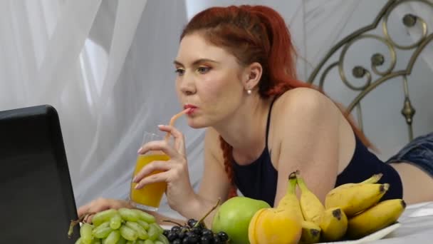 Jovem desfrutando em uma cama, usando laptop e bebidas suco de laranja. câmara lenta — Vídeo de Stock