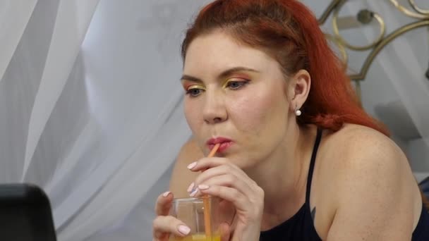 Ung kvinna njuter på en säng, med laptop och dricker apelsinjuice. slowmotion — Stockvideo