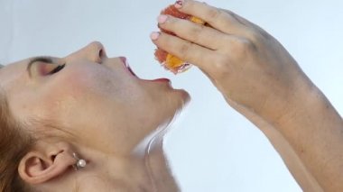 Genç kadının ağzına ve beyaz bir arka planda yavaş boynundaki portakal sıkma