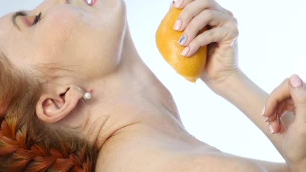 Jeune femme serrant l'orange dans la bouche et sur votre cou sur un fond blanc, au ralenti — Video