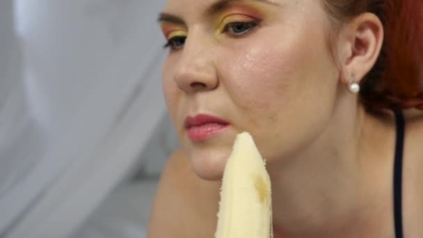 Mujer joven disfrutando en una cama, utilizando el ordenador portátil y comer un plátano en casa por la mañana. cámara lenta — Vídeos de Stock