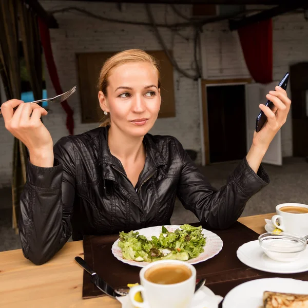 実業家の屋外カフェでサラダを食べるします。健全な生活様式: あなたの携帯電話で緑のおいしい食べ物やチェック メールを食べる女の子 — ストック写真