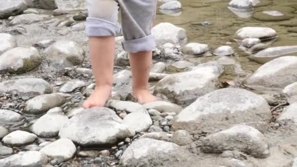 Feet of little girl run barefoot on a stone beach by the lake. slow motion — Stock Video