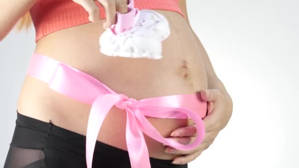 Zwangere mama in ondergoed spelen met baby laarsjes. buik met roze lint. Slow motion — Stockvideo