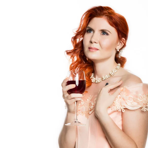 Молодая рыжая мечтательная женщина пьет красное вино со счастливым лицом и улыбается. Белый фон. свободное место для текста — стоковое фото