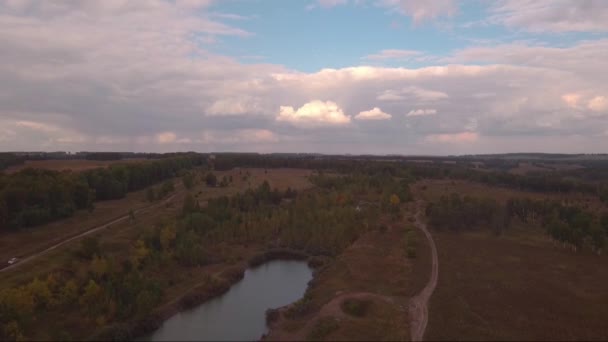 Vista aérea: Vuelo sobre un camino de campo con un pequeño lago, nubes de tormenta en el horizonte — Vídeos de Stock