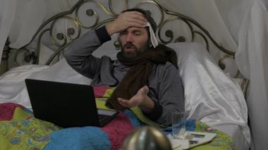 Hasta bir adam sıcak bir eşarp ile bir yatakta boynunu ve bir havlu çevresinde onun baş, video doktor bir dizüstü bilgisayarda sohbet üzerinde yatıyor. ağır çekim