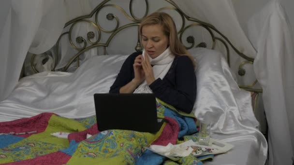 Женщина брызгает лекарством в нос. Назальный спрей. Девушка лежит в постели с теплым шарфом на шее. 4K — стоковое видео