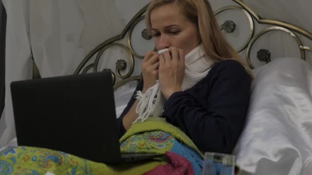 Een zieke vrouw videochat met je arts op een laptop. meisje ligt in een bed met een warme sjaal om zijn nek. Slow motion — Stockvideo