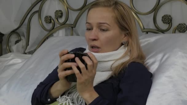Nemocná žena leží na posteli doma a pije horký nápoj s medem. 4k — Stock video