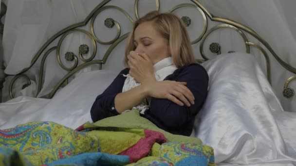Sjuk kvinna hosta och drycker ett piller. flicka ligger i en säng med en varm halsduk runt halsen. 4k — Stockvideo
