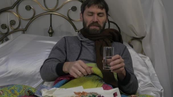 Egy beteg ember fekszik egy ágyban egy meleg sál a nyakában, köhögés és italok a tabletták. lassú mozgás — Stock videók